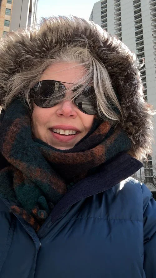 Deborah Libby smiling in sunglasses and a fur-lined winter hood on a Chicago street