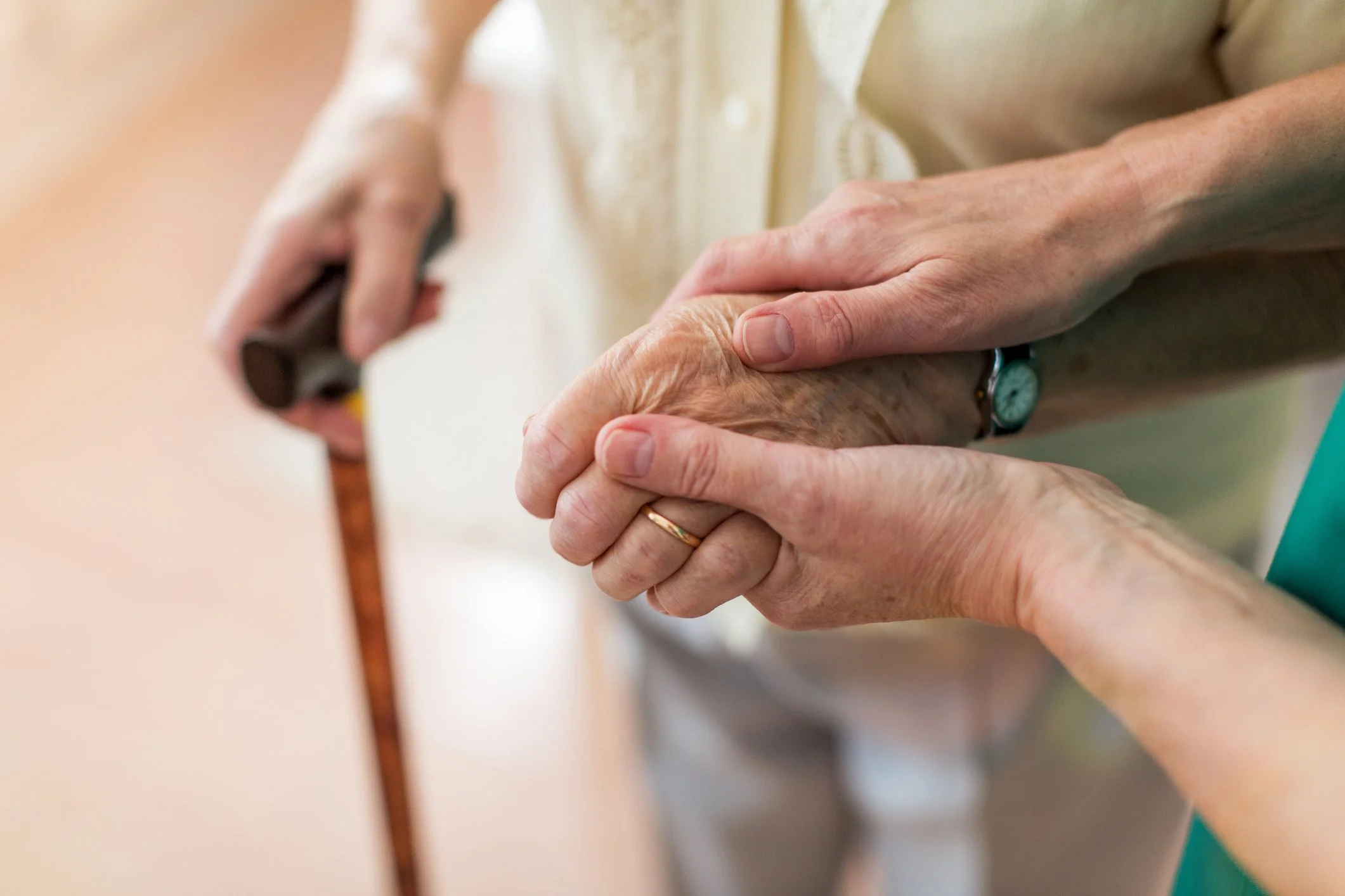 A caring hand resting on an older person's hand as they hold a wooden cane
